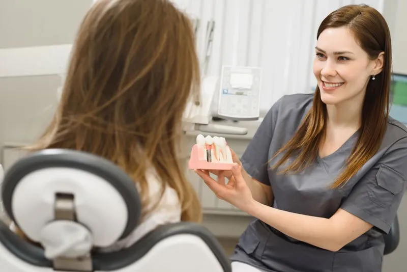 a trusted doctor showing a dental implant model to a patient so she can point out how exactly dental implants can benefit her smile.