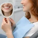 Young Redhead Woman Admiring Her Smile in Handheld Mirror, Dental Patient