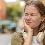 Portrait of young Caucasian woman standing outdoors feeling toothache bad unpleasant symptoms suffering from pain holding hand on cheek jaw damaged dental nerve needs medical help. Girl on city street