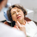 Senior woman pointing at her teeth while talking to dentist